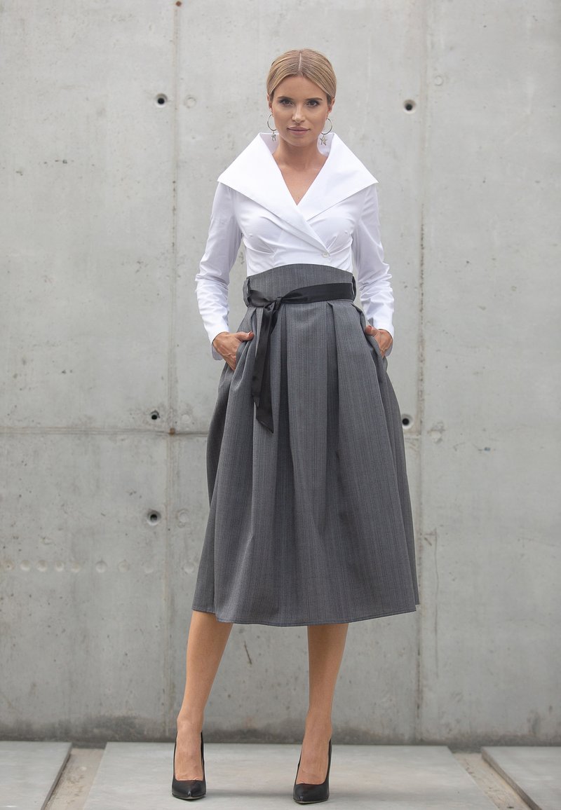 Biała bluzka z długim rękawem i dużym kołnierzem, zestawiona z szaro plisowaną spódnicą z kieszeniami i czarnym paskiem wstążkowym. Szpilki.