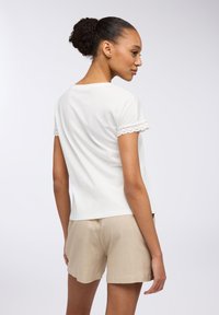 Biała bawełniana koszulka z koronkowymi wykończeniami na rękawach, zestawiona z beżowymi lnianymi szortami. Gładka tekstura, luźny krój i prosty design.