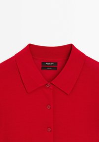 Röd ullpolotröja med klassisk krage, två knäppningar och en mjuk textur. Etiketten säger "Massimo Dutti, tillverkad i Indien."