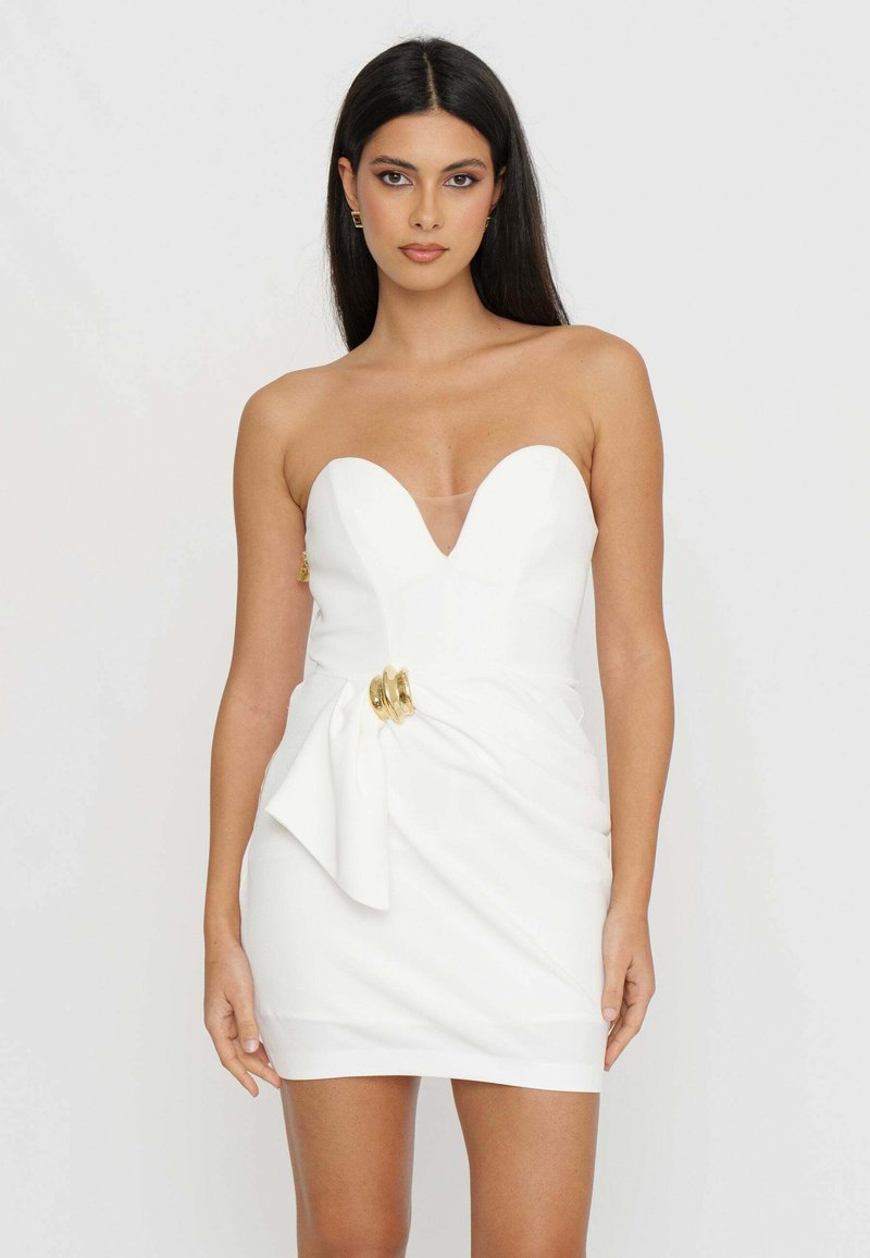 Abito bianco senza spalline con scollatura a V profonda, presenta un dettaglio in vita annodato e accenti dorati. Tessuto morbido e silhouette aderente.