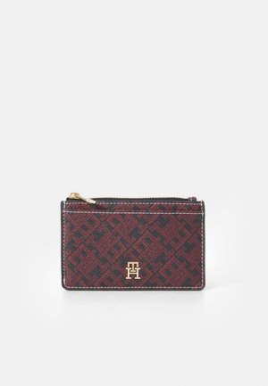 Red and black patterned cardholder made of textured material, with a gold logo and a zip closure along the top edge.