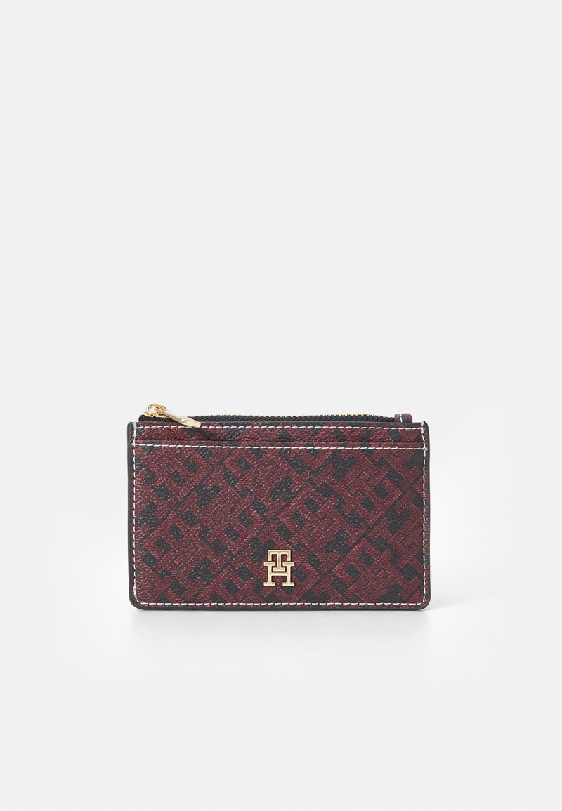 Red and black patterned cardholder made of textured material, with a gold logo and a zip closure along the top edge.