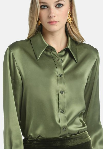Satenasta maslinasto zelena bluzica s oštrim ovratnikom, dugim rukavima i kopčanjem sprijeda. Glatka tekstura i suptilni sjaj su istaknuti detalji.