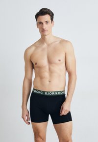 Fekete férfi boxeralsó zöld derékkal, rajta fehér "BJÖRN BORG" felirattal. Az anyaga simának tűnik, fitted kialakítással.