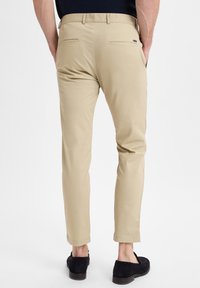 Beige chino's met een slim fit, voorzien van twee achterzakken en een soepele stoftextuur. De zoom is licht taperend. G gedragen met donkere schoenen.