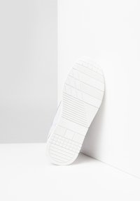 Suola di sneaker bianca con un motivo texturizzato, caratterizzata da accenti grigio chiaro e rosa lungo i lati e una superficie superiore liscia.