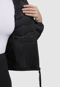 Czarna kurtka puchowa, charakteryzująca się pikowanym teksturem, zamkiem błyskawicznym i czarnym elastycznym dołem. Wnętrze z gładką podszewką bez widocznych wzorów.