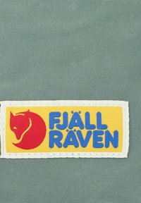 Geweven patch met een rode vos icoon en "FJÄLL RÄVEN" in het blauw, geplaatst op een textuurachtige groene achtergrond met een gele rand.