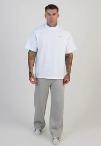 Vit bomulls-T-shirt med korta ärmar, polokrage och diskret logotyp. Matchas med ljusgrå mjukisbyxor med avslappnad passform och mjuk textur.