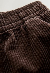 Close-up of dark brown ribbed corduroy fabric with elastic waistband and gathered stitching.