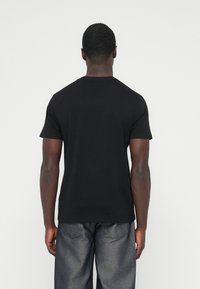 Μαύρο κοντομάνικο μπλουζάκι από βαμβάκι, με στρογγυλή λαιμόκοψη και απλό σχέδιο. Φορεμένο με σκούρο γκρι τζιν παντελόνι.