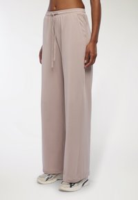 Jasno beżowe dresy z elastycznym pasem, detalami w postaci sznurka i bocznymi kieszeniami. Miękki, zwiewny materiał o szerokim kroju nogawek.