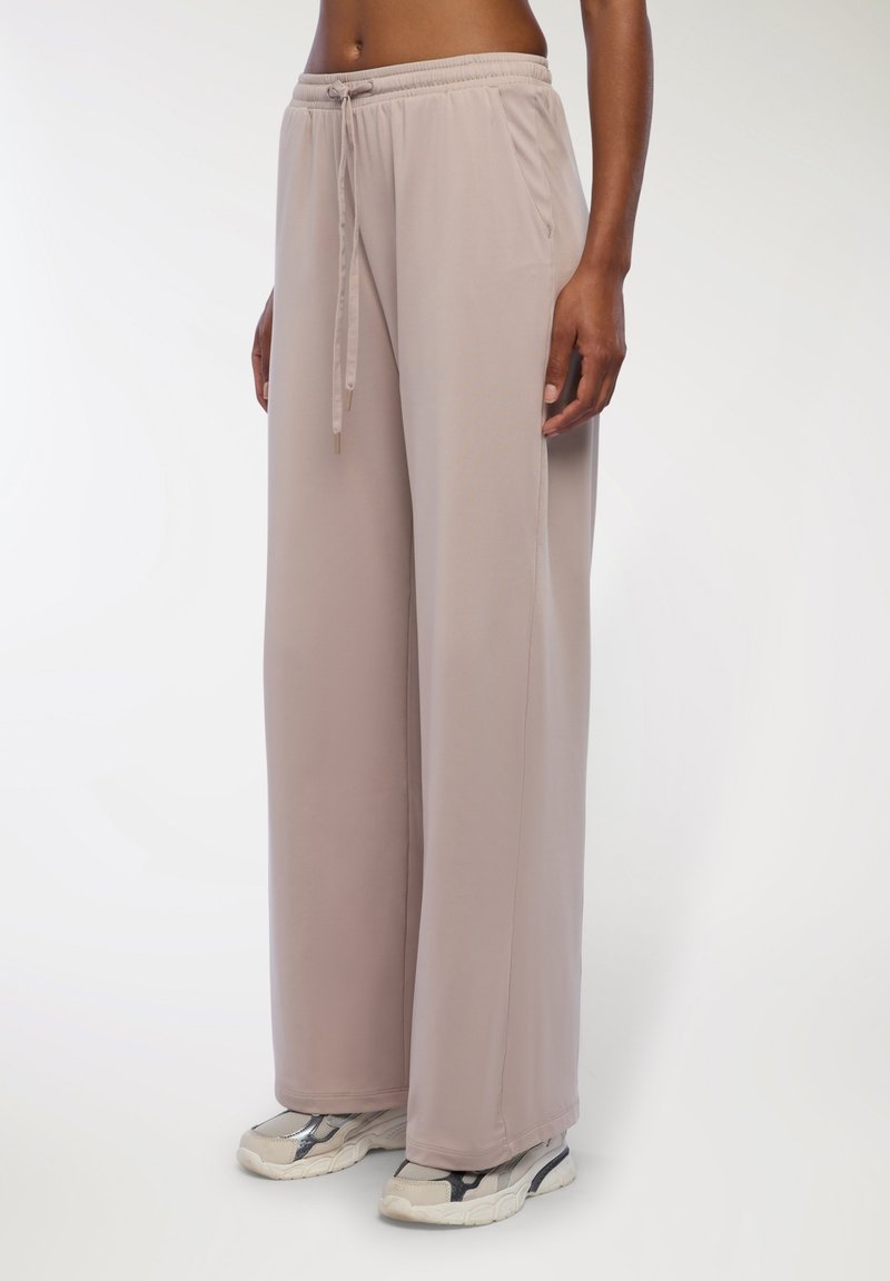 Jasno beżowe dresy z elastycznym pasem, detalami w postaci sznurka i bocznymi kieszeniami. Miękki, zwiewny materiał o szerokim kroju nogawek.