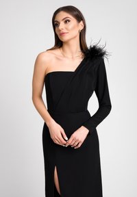 Czarna wieczorowa suknia z asymetrycznym rękawem, dopasowanym topem, długim rękawem i akcentem z piór. Zawiera rozcięcie do uda i gładką fakturę.