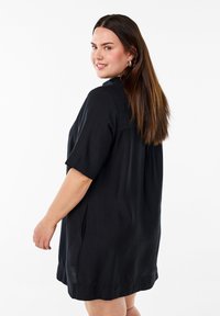 Schwarzes Kurzarmkleid aus glattem, leichtem Stoff. Bietet eine lockere Passform und eine subtile Textur mit seitlichen Schlitzen am Saum.