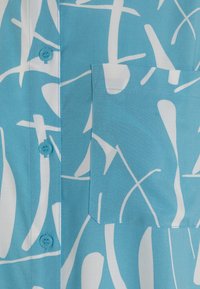 Short-sleeve shirt in light blue fabric featuring abstract white patterns, one button, and a patch pocket on the left side.