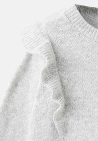 Szary sweter dzianinowy z prążkowanym dekoltem i falbaniastym akcentem na ramieniu. Tekstura jest miękka z delikatnymi detalami w formie błysku.