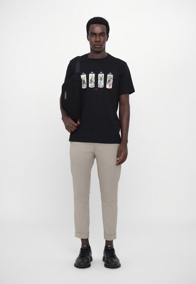 Black T-shirt with graphic print of colorful spray cans, beige trousers, and black sneakers. Distinct shapes and minimal texture details.