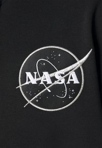 Tela negra con un logo de NASA bordado. El logo incluye un diseño circular con estrellas y una trayectoria orbital.