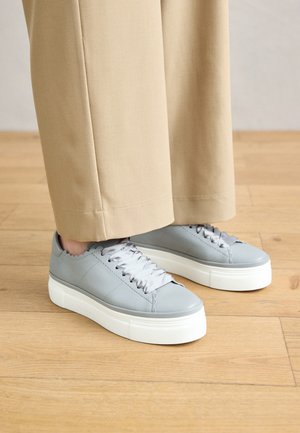 Grijze leren sneakers met een textuurafwerking en gegolfde randen. Voorzien van witte platformzolen en satijnen grijze veters. Draag ze met beige broeken.