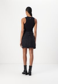 Svart ärmlös topp, svart denim minikjol med fickor, och svarta ankelstövlar, sedd bakifrån mot en vit bakgrund.