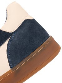 Close-up of beige and navy suede sneaker heel with brown rubber sole and visible stitching details.