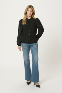 Black blouse with sheer puff sleeves and gold buttons, paired with light blue flared jeans and black patent leather heels.