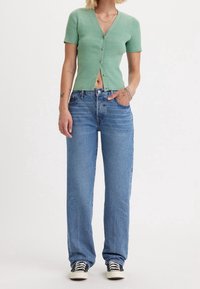 Green ribbed short-sleeve cardigan with button closure, paired with light blue wide-leg jeans and black-and-white sneakers.