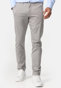 Chino gris clair avec une coupe slim, fabriqué en tissu mélange de coton. Dispose de poches latérales et d'une texture lisse. Associé à des baskets blanches.