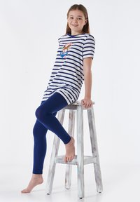 Koszulka z krótkim rękawem w paski z graficznym wzorem, w komplecie z niebieskimi legginsami. Koszulka ma okrągły dekolt i luźny krój.