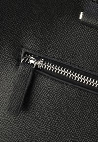Material de cuero negro texturizado con un cierre plateado brillante. Presenta un tirador rectangular para el cierre y un acento suave cerca del zipper.
