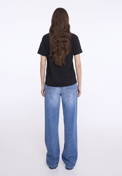 Tricou negru cu mânecă scurtă, asortat cu blugi deschiși, cu croială largă. Blugii au un design clasic cu cinci buzunare și detalii decorative de cusătură.