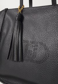 Borsa a tracolla in pelle nera con texture, caratterizzata da un accento con pon-pon e un design del logo perforato sulla parte anteriore, con manici robusti e accessori in oro.