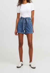 Denim shorts with a high waist, featuring a tie belt, rolled hem, and four pockets. Paired with a fitted white t-shirt and sneakers.