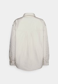 Lichtbeige overhemd met een licht gekreukte textuur, een brede kraag, lange mouwen en knoopmanchetten, met een rechte achternaad.