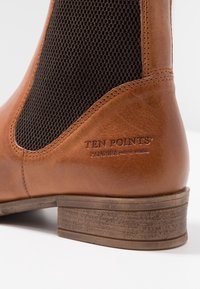 Brązowy skórzany botek za kostkę z teksturowanym panelem z ciemno brązowej siateczki. Posiada niski, zdobiony obcas oraz tłoczone logo po bokach.