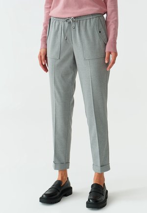 Femme portant un pantalon gris clair fuselé avec poches plaquées devant, revers roulés, un pull rose et des mocassins en cuir noir.