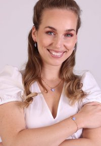 Gouden sieradenset met lichtblauwe hartvormige hangers in oorbellen en een ketting, met een bijpassende armband. Model draagt een witte blouse.