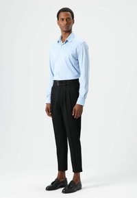 Chemise bleu clair à manches longues avec un col pointu, associée à un pantalon noir taille haute doté d'un double détail de boucle et de jambes effilées.