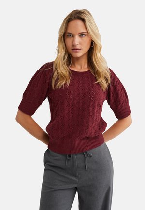 Bordeaux kortærmet strikket sweater med diamantmønstre og ribbede kanter, parret med grå stribede bukser.