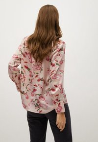 Blouse à manches longues en tissu rose, avec un motif floral dans des tons de rouge et blanc, une coupe décontractée et un léger brillant.