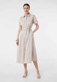 Helles beiges Hemdkleid aus glattem Stoff, mit einem taillierten Gürtel, kurzen Ärmeln, Knopfverschluss und seitlichen Taschen.