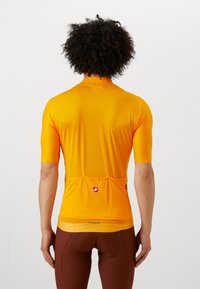 Maillot de cyclisme à manches courtes de couleur orange vif, avec un tissu texturé, des poches arrière et une étiquette de logo près de l'ourlet.
