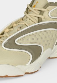 Gros plan d'une basket en cuir beige et taupe avec une semelle blanche et en caoutchouc, une couture détaillée et des lacets épais beige.