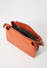 Orange läderhandväska med texturerad yta, dragkedjestängning och innerficka. Utrustad med giltiga detaljer och dubbla bärhandtag.