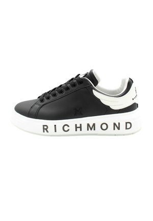Zapatilla baja negra con suela blanca que presenta el texto "RICHMOND", cordones negros y detalle de ala blanca en el cuello del talón.