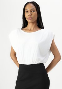 Blouse blanche à manches courtes avec un col arrondi et une taille froncée, associée à une jupe noire ajustée. Tissu lisse avec une coupe décontractée.
