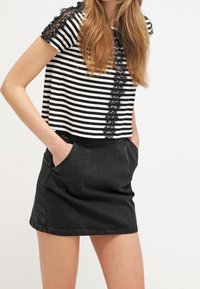 Černá džínsová sukně se bočními kapsami, spárovaná s croptopem s černobílými pruhy a krajkovými detaily na ramenech.