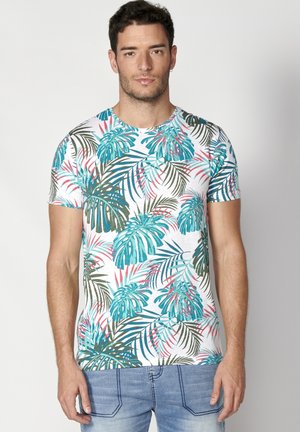 T-shirt à manches courtes en coton, avec une base blanche ornée d'un imprimé de feuilles tropicales colorées dans des teintes de bleu canard, vert et rose.