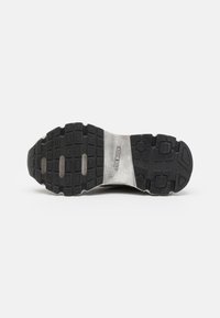 Soletta di sneaker nera con battistrada in gomma testurizzata, dotata di un sottile strato metallico argento e marchio impresso sul lato.